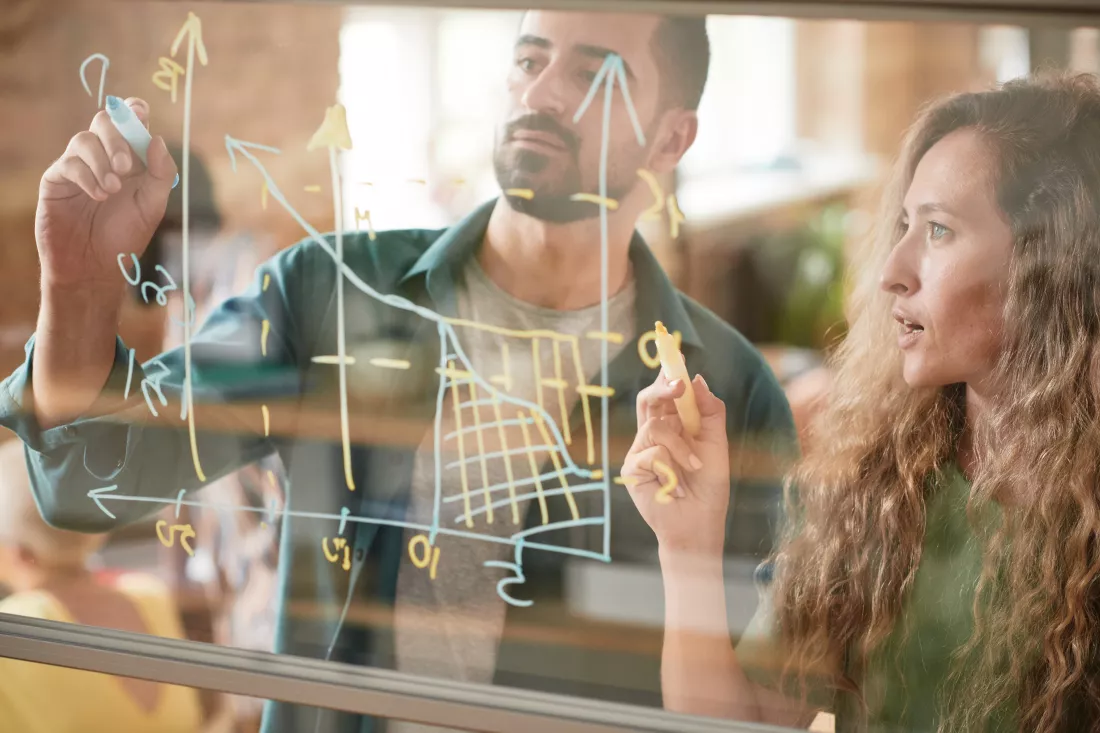 business-colleagues-drawing-financial-graphic-glass-wall-examining-it-together-team-presentation-office